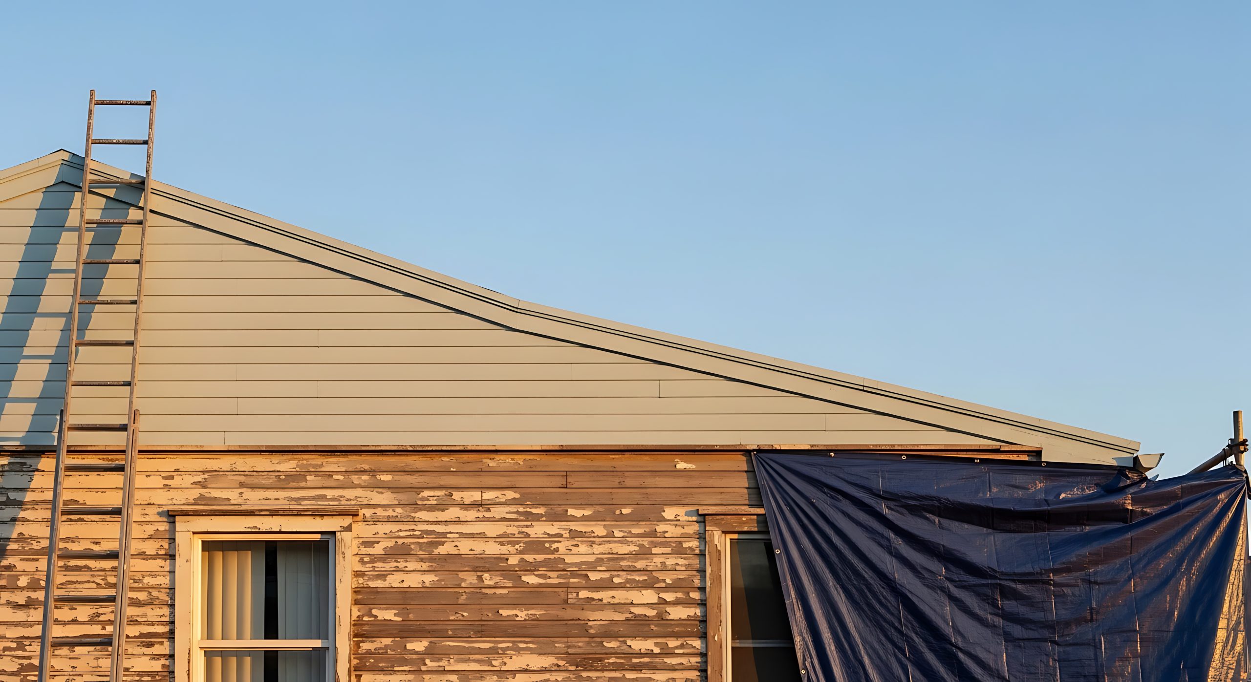 Fixer upper house exterior showing old wood siding with peeling paint and a ladder against the new roof during a residential home renovation project Modern Okanagan home with dark corrugated metal panel and wood-accent siding installed by Hi-Lite Exteriors