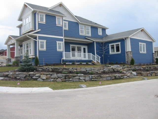 Hi-Lite Exteriors royal blue siding Two-storey blue siding home with white trim, covered front porch, and stone retaining wall landscaping in the Okanagan
